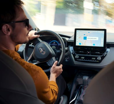 En man i en organge tröja svänger till höger i sin Toyota. Bilen Multimediaskärm visar att en uppdatering laddas ned.