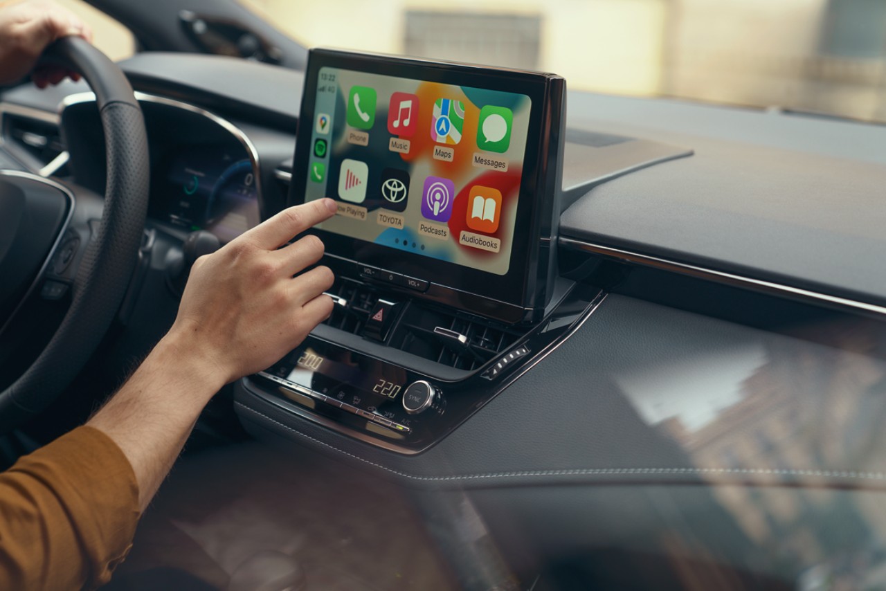 En person sitter i en Toyota och använder sig av Multimedia-skärmen och dess Uppkopplade tjänster.. Skärmen visar hemskärmen för Apple CarPlay.