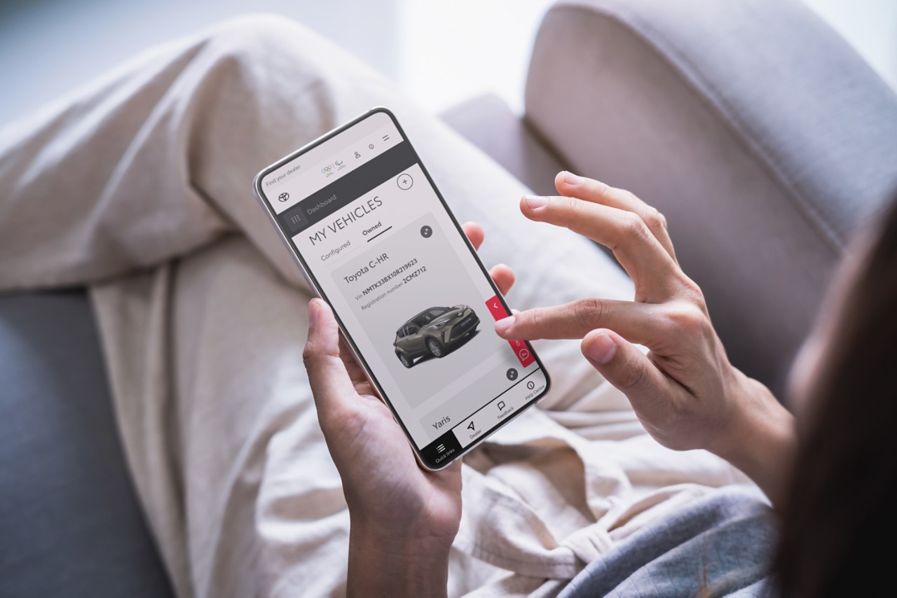 En kvinna använder sin mobiltelefon. Den visar en Toyota C-HR på Mina bilar-sidan i MyToyota kundportalen.